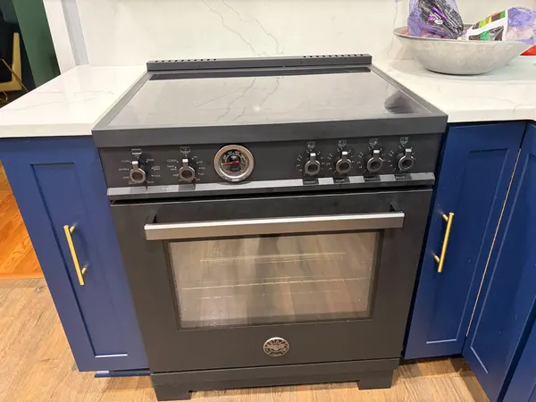 Matte black Bertazzoni range with a glass cooktop, a temperature gauge and a single oven, between blue cabinets