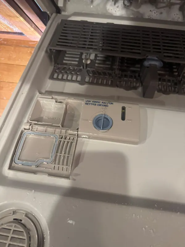 Detergent cup and rinse-aid dispenser on the inside of a dishwasher door, labeled Use rinse aid for better drying