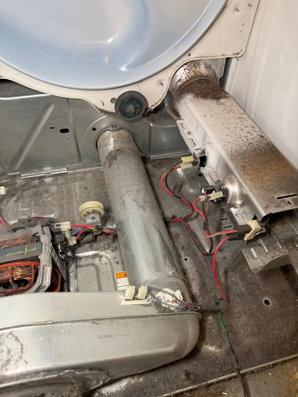 Lint packed around the heater housing and blower duct inside an opened dryer