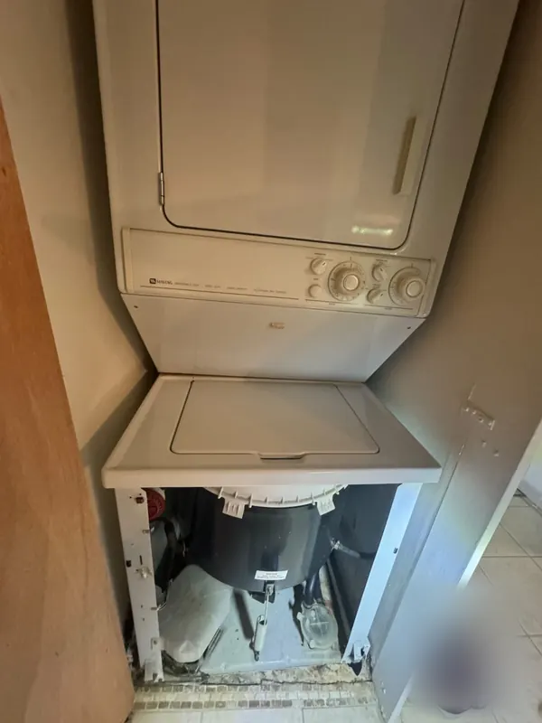 Older Maytag stacked laundry center in a closet, the washer's front panel removed to reach the tub and motor