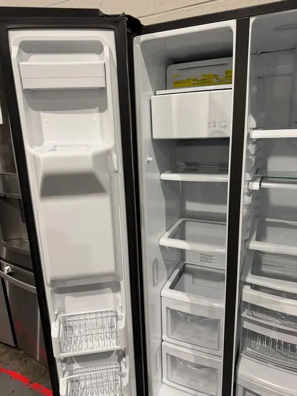 Freezer side of a side-by-side refrigerator with the dispenser door open and the ice maker at the top