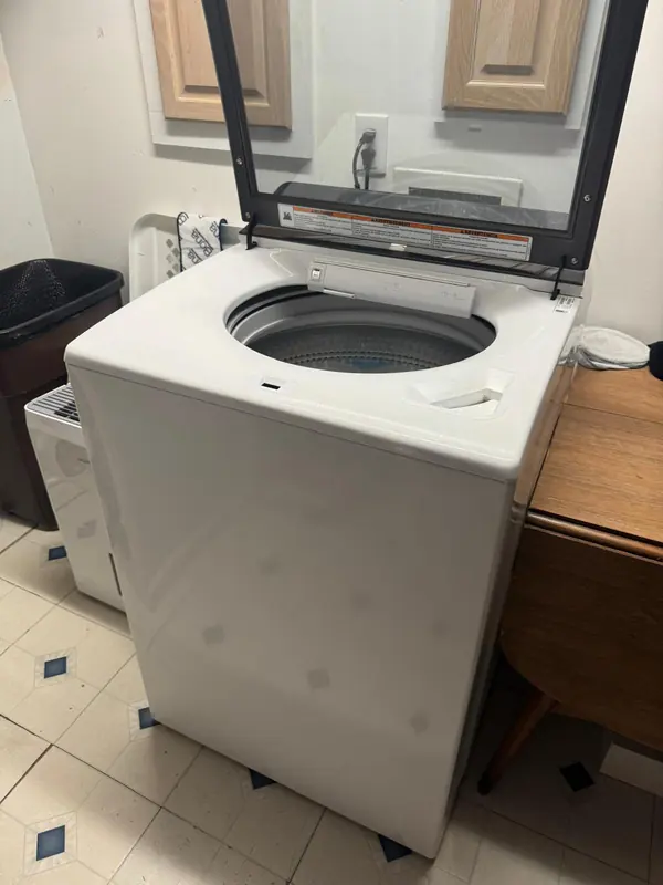 White top-load washer with the glass lid raised, showing the wash basket and dispensers