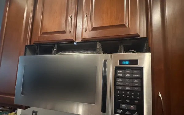 Whirlpool Gold over-the-range microwave with its top vent grille removed, between wood cabinets