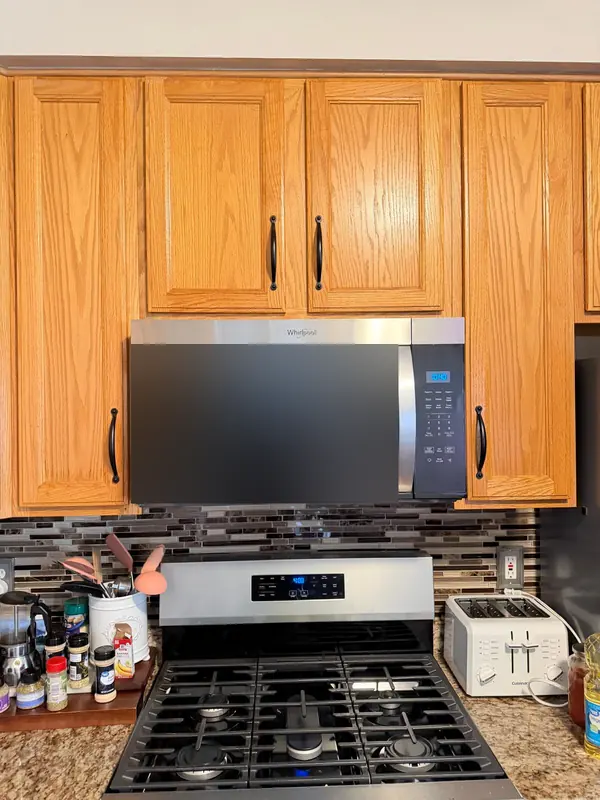 Whirlpool over-the-range microwave mounted between oak cabinets above a gas range