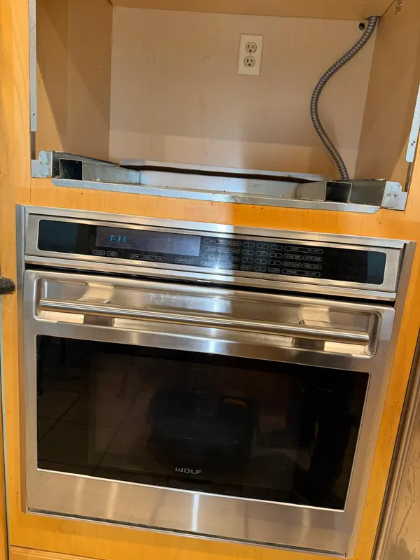Wolf built-in wall oven with the cabinet opening above it exposed, showing the mounting rails, an outlet and armored cable